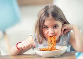 Cute little kid girl eating spaghetti bolognese at home.