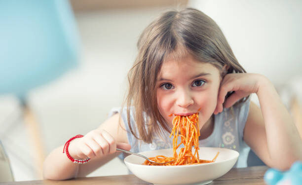 Cute little kid girl eating spaghetti bolognese at home.