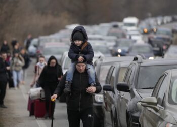 Ukrainian refugees walk along vehicles lining-up to cross the border from Ukraine into Moldova, at Mayaky-Udobne crossing border point near Mayaky-Udobne, Ukraine, Saturday, Feb. 26, 2022. The U.N. refugee agency says nearly 120,000 people have so far fled Ukraine into neighboring countries in the wake of the Russian invasion. The number was going up fast as Ukrainians grabbed their belongings and rushed to escape from a deadly Russian onslaught. (AP Photo/Sergei Grits)